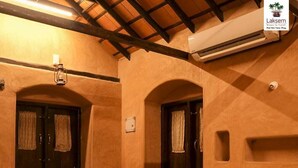 Habitación de hotel con dos camas individuales, un banco, una ventana con cortinas, un equipo de aire acondicionado y una lámpara fijada a la pared.