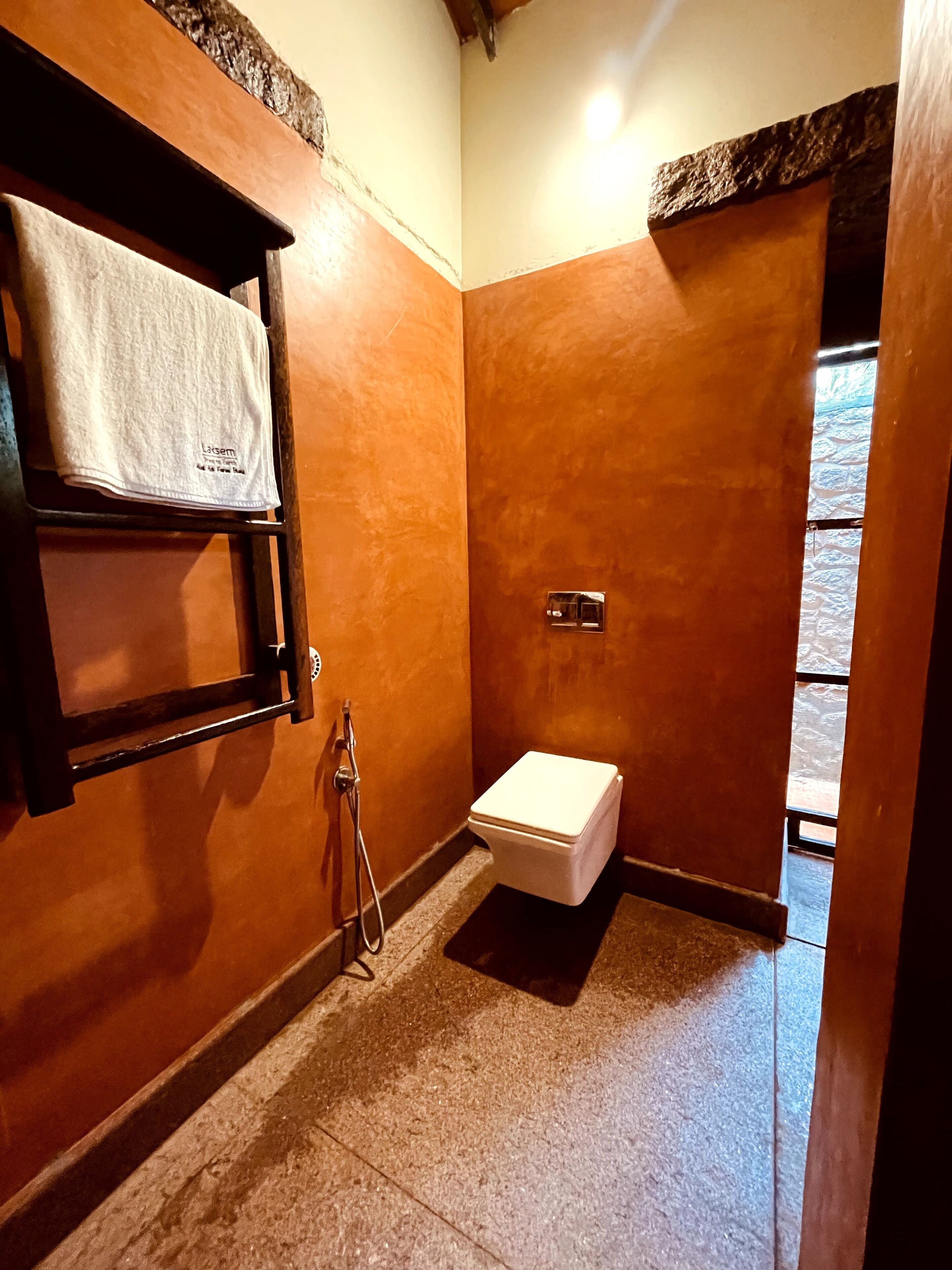 A small bathroom with a toilet, a towel hanging on a rack, and a shower head.