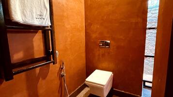 Un baño pequeño con inodoro, una toalla colgada en un perchero y un cabezal de ducha.