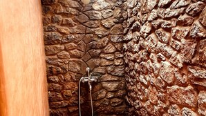Zona de ducha con paredes de piedra, un cabezal de ducha y un lavabo metálico.