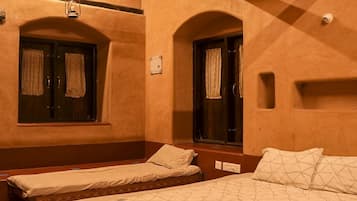 A hotel room with two single beds, a bench, a window with curtains, an air conditioning unit, and a wall-mounted light fixture.