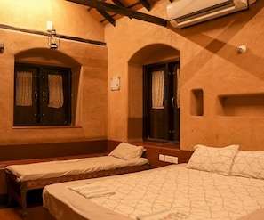 A hotel room with two single beds, a bench, a window with curtains, an air conditioning unit, and a wall-mounted light fixture. - Down to Earth Farmstay by LAKSEM (Anaimalai)