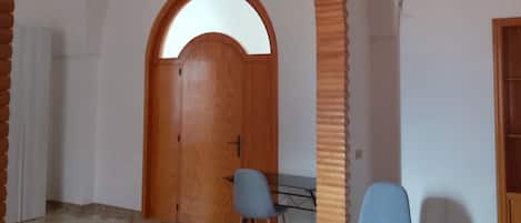 A room with a high arched doorway, a wooden door, a table with chairs, and a patterned floor.