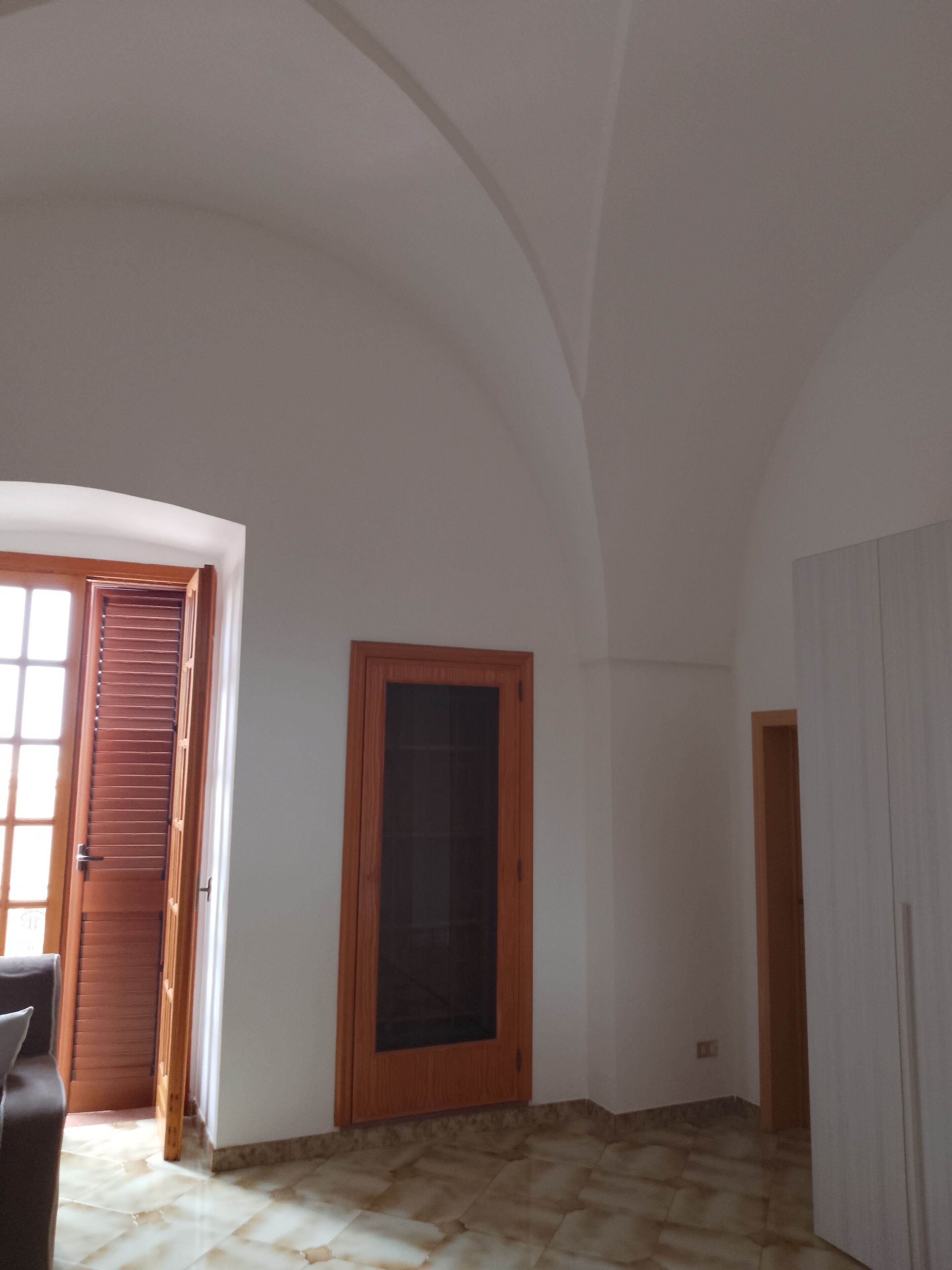 Una habitación con techo abovedado, puerta de madera, ventana y suelo de baldosas.