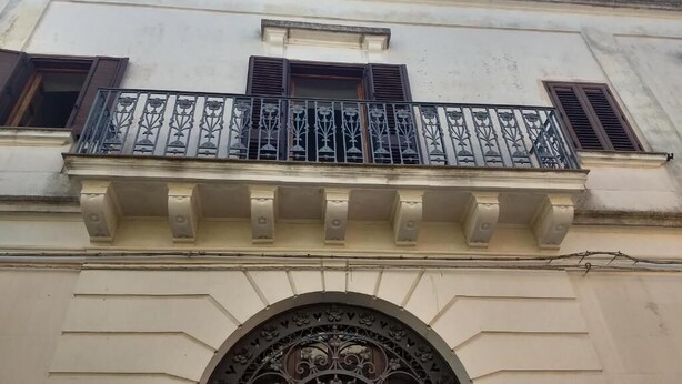 A building facade with a balcony featuring ornate metal railings and a decorative archway with the letters "DBR" above the entrance. - Salento Relax Cinzia Room (Collepasso)