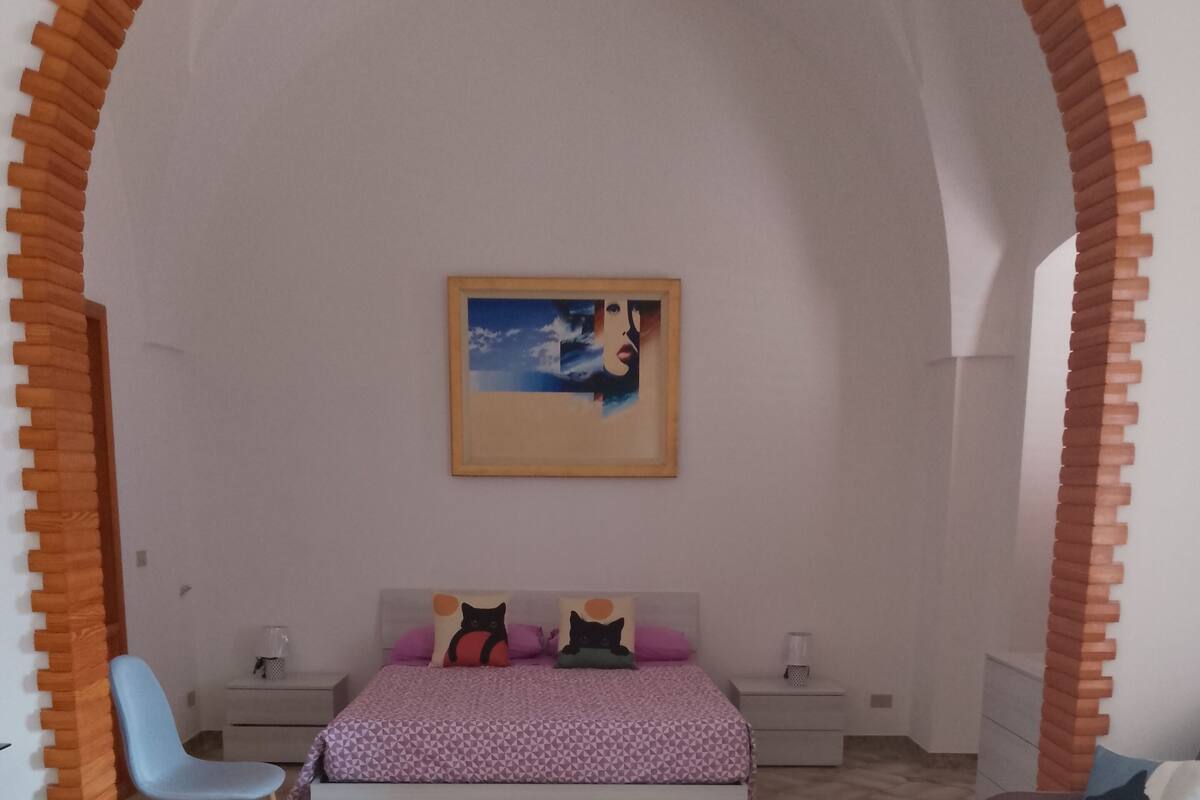 A bedroom with a bed, two chairs, a couch, a painting on the wall, and a tiled floor.