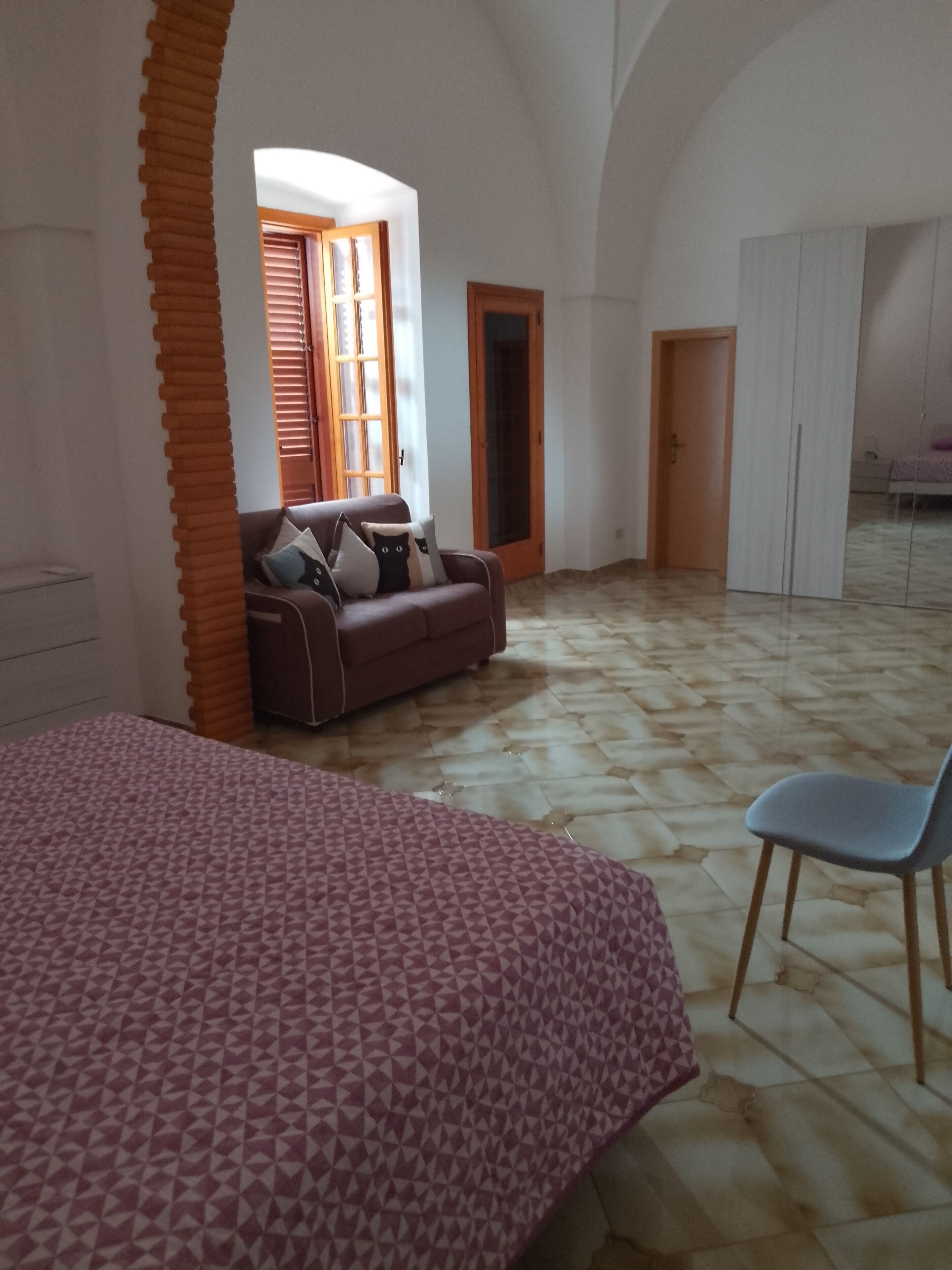 Een kamer met een bed met patroon, een bank met kussens, een stoel en een betegelde vloer.