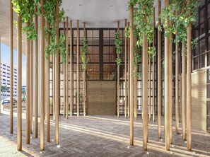 A modern building entrance with vertical bamboo poles and green plants.