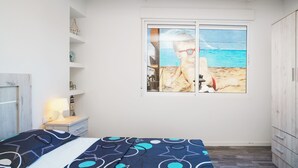 Una camera da letto con un letto, un comodino, un armadio e una finestra vista spiaggia.