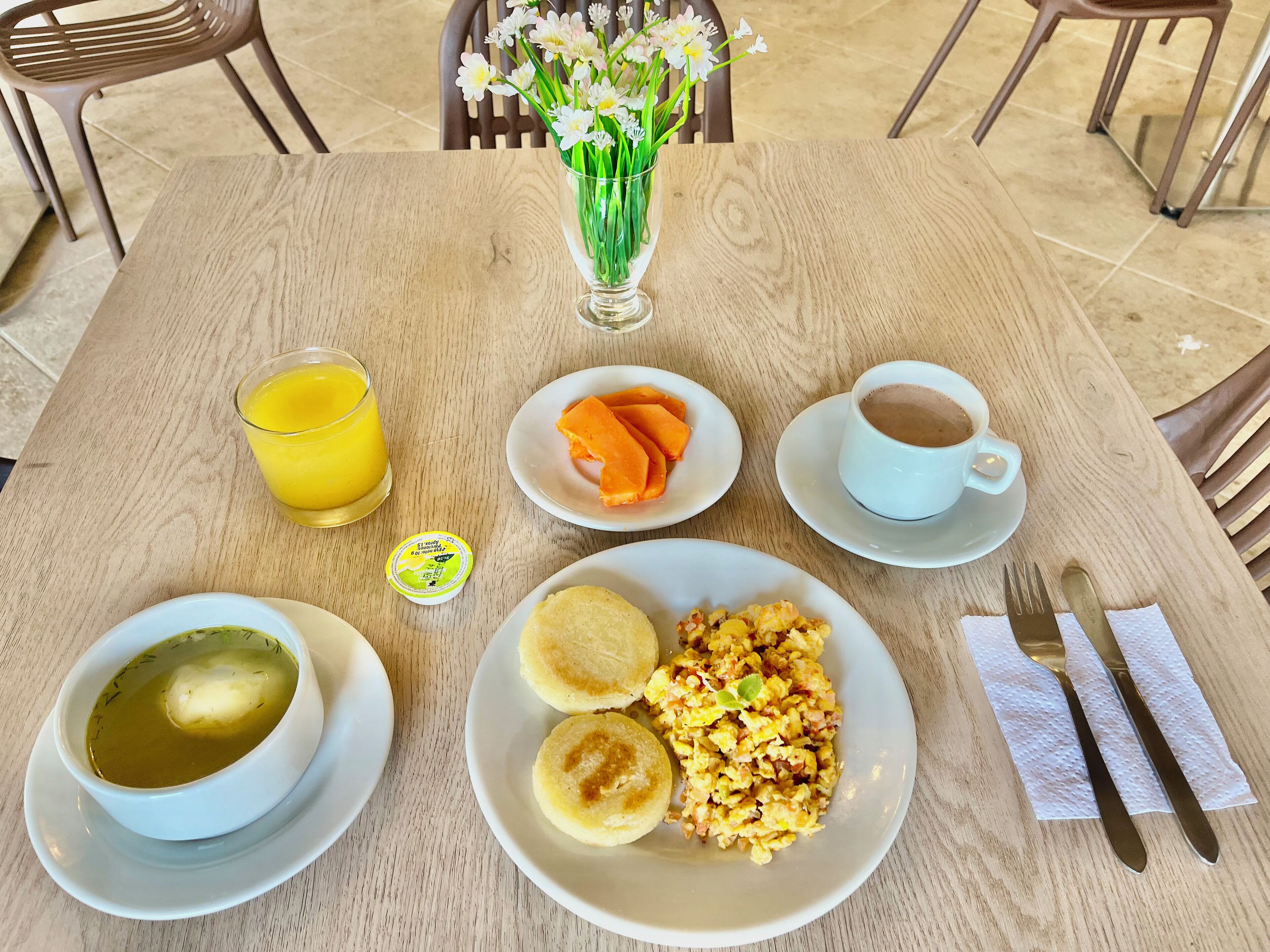 Een houten tafel met ontbijtartikelen zoals sinaasappelpartjes, roerei en een kop koffie.