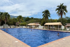 A swimming pool with a tiled edge, surrounded by palm trees and a mountain backdrop. - Hotel Las Palmeras (Villeta)
