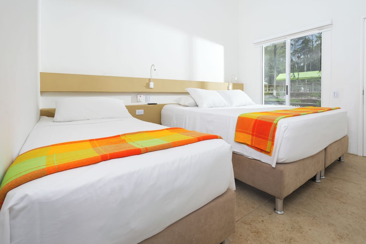 Habitación de hotel con dos camas, un ventanal grande y vistas al exterior.