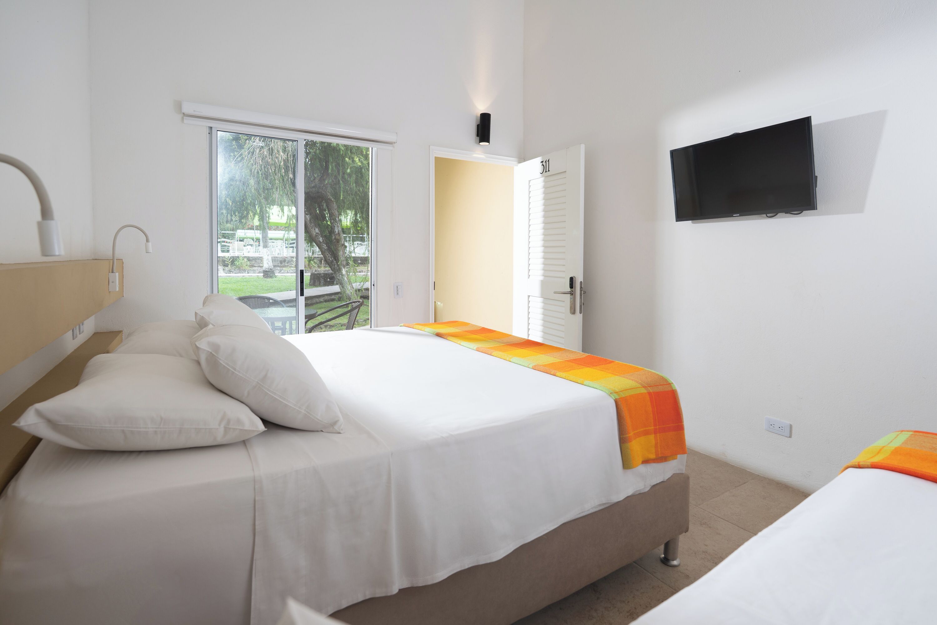A bedroom with a bed, a TV mounted on the wall, and a door leading to an outdoor area.