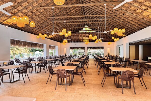 Un vaste espace de restauration intérieur, doté de nombreuses tables et chaises, d’un plafond en bois et de luminaires suspendus.