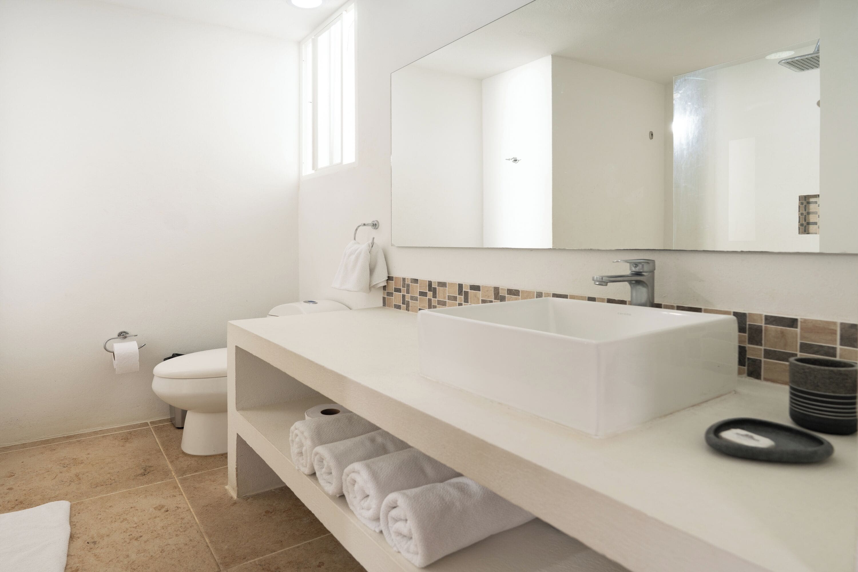 Een moderne badkamer met een witte wastafel, een grote spiegel en een toilet.