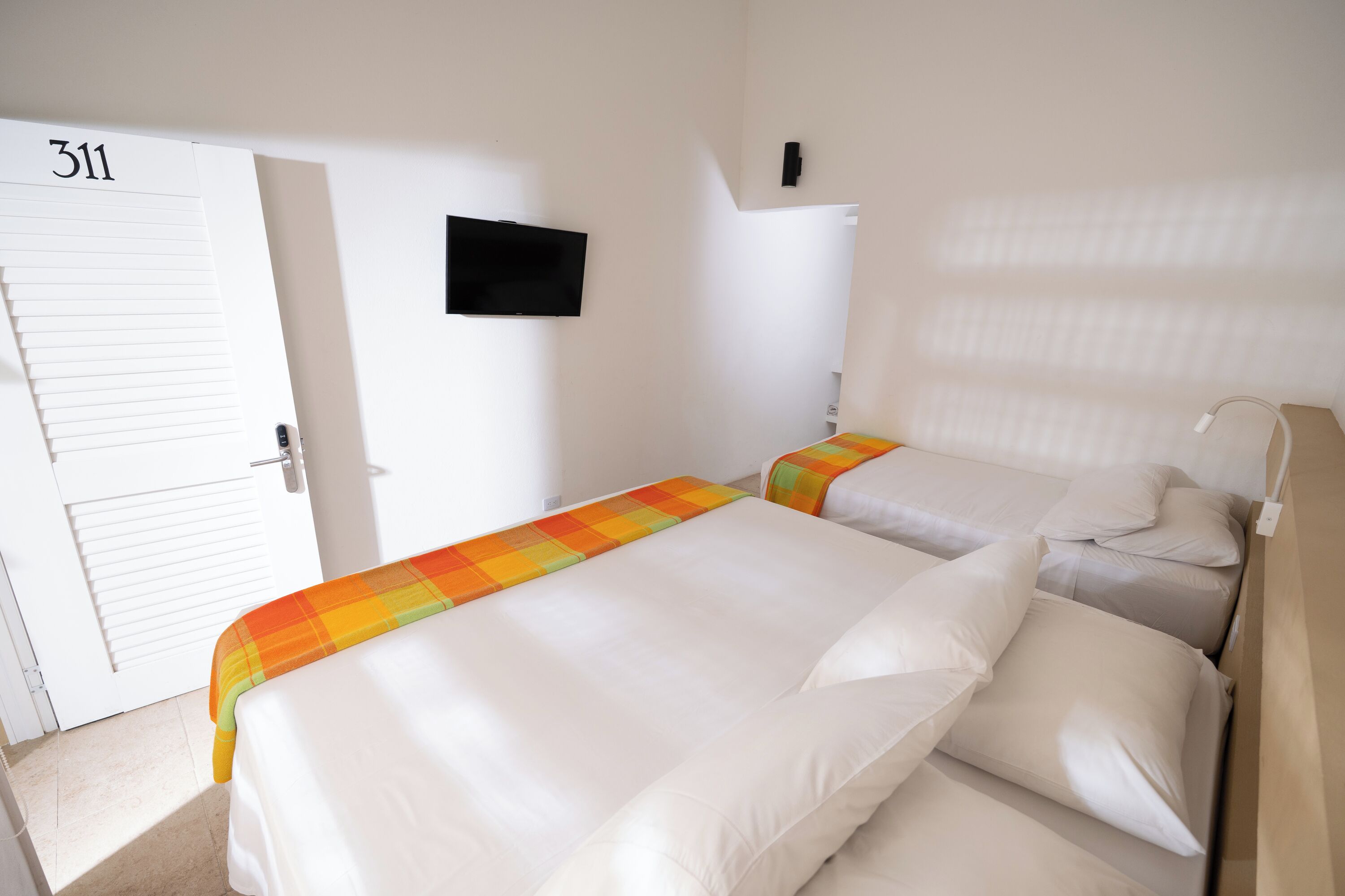 Habitación de hotel con dos camas, un televisor en la pared y una puerta con el número 311.