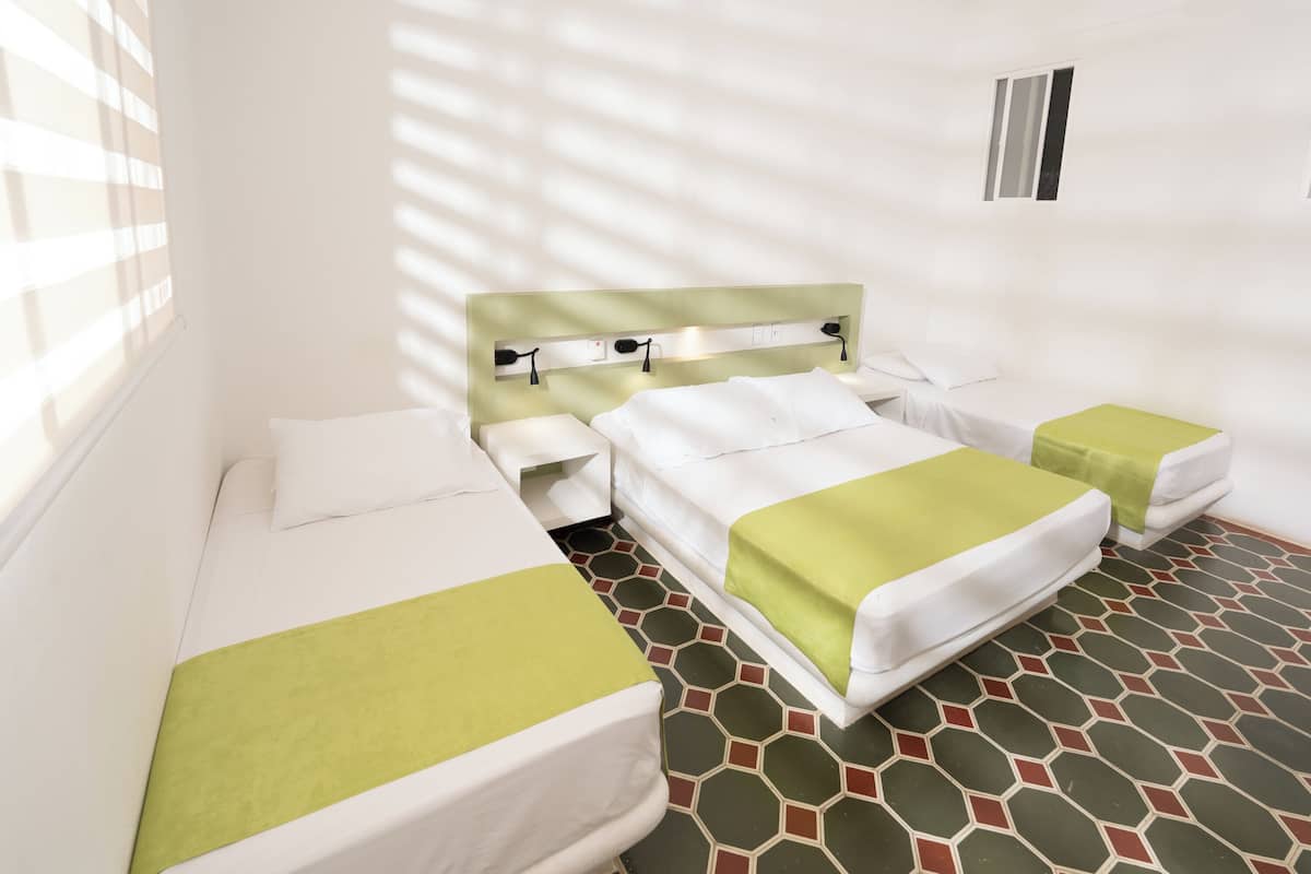 Una habitación de hotel con dos camas individuales, una mesita de noche pequeña y una ventana con persianas.