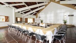 Een vergaderruimte met lange tafels en stoelen, witte muren en een hoge plafond met zichtbare balken.