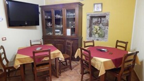 A dining area with two tables, wooden chairs, a television, a cabinet with glass doors, and a stone wall with a vase. - La collinettabeb (Bisignano)