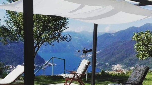 A sunlit outdoor seating area with a view of mountains and a lake. - La collinettabeb (Bisignano)