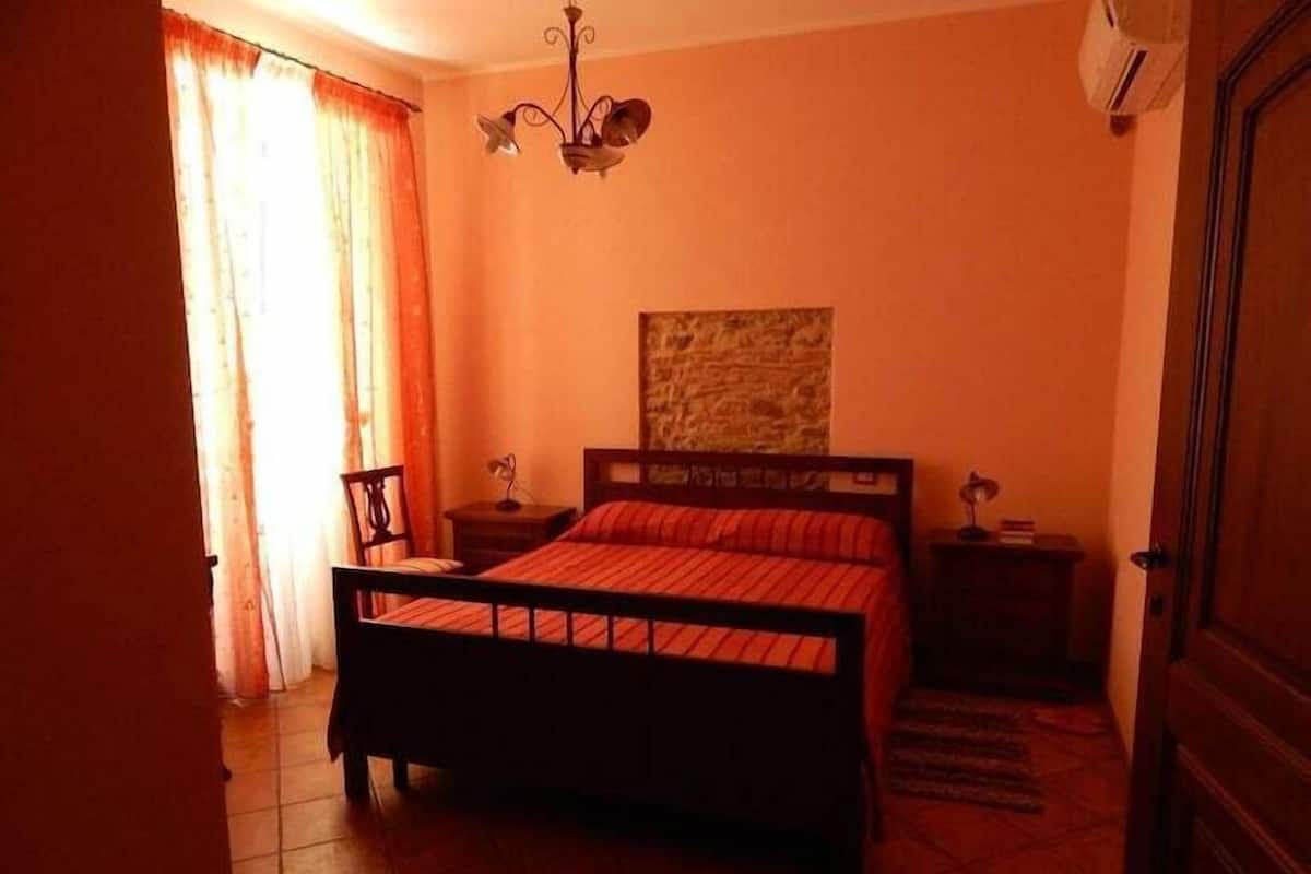 A bedroom with a bed, a nightstand, a lamp, a wall-mounted artwork, and a door.