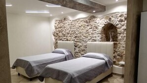 A modern room with two beds, a stone wall, and recessed lighting. - La collinettabeb (Bisignano)