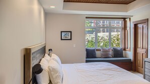 A bedroom with a bed, a window seat with cushions, a framed picture on the wall, and a wooden headboard. -  365 Moonshine Crescent by Okanagan Premier (Beaverdell)