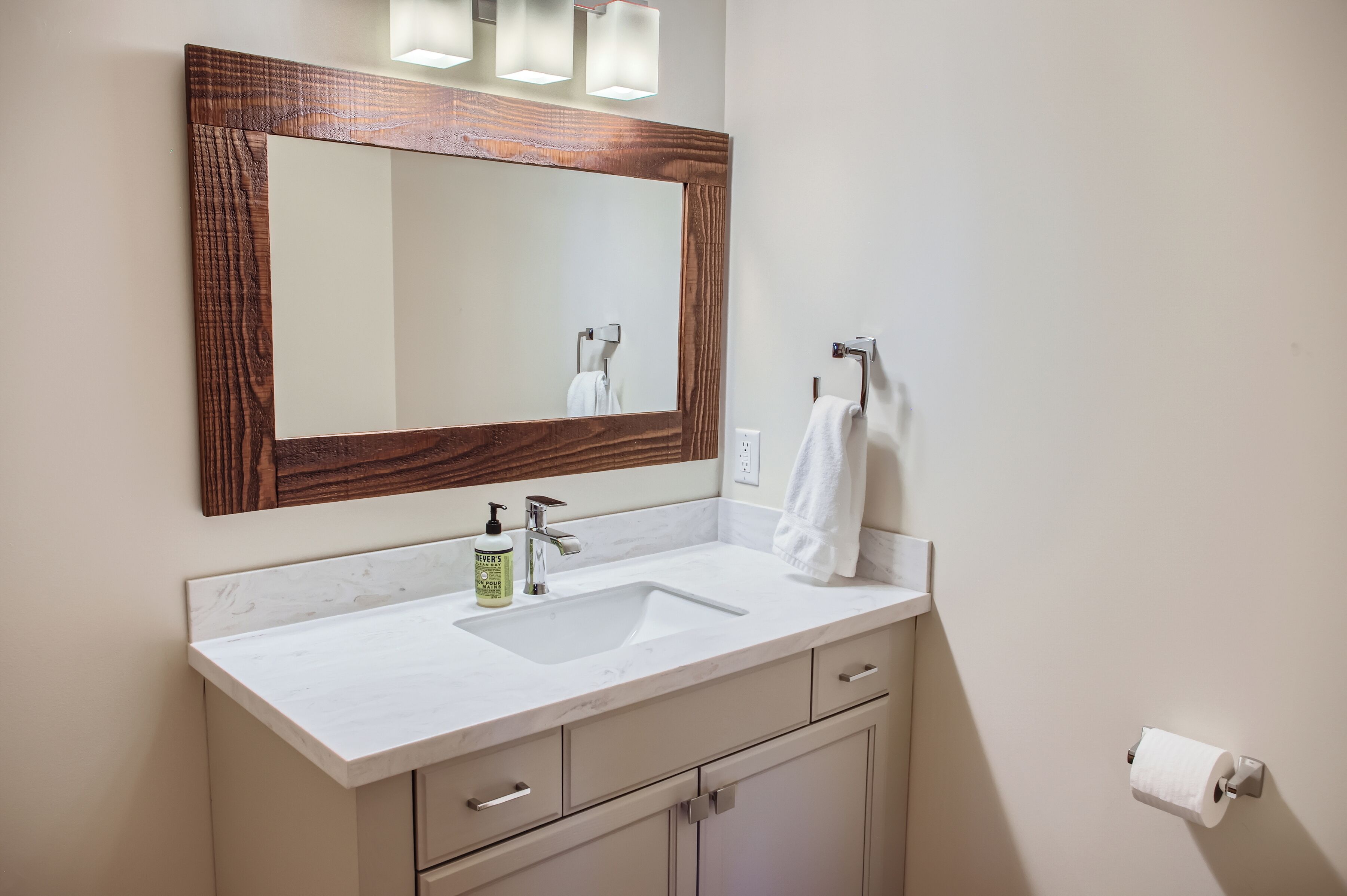 A bathroom with a large mirror, a sink, a towel rack, and a toilet paper holder.