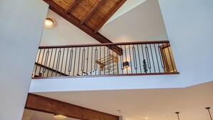 A multi-level interior with exposed wooden beams, a balcony with metal railings, and recessed lighting. -  365 Moonshine Crescent by Okanagan Premier (Beaverdell)