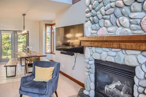 Una sala de estar moderna con chimenea de piedra, un televisor de pantalla plana montado encima y una zona de comedor con mesa y sillas de madera.