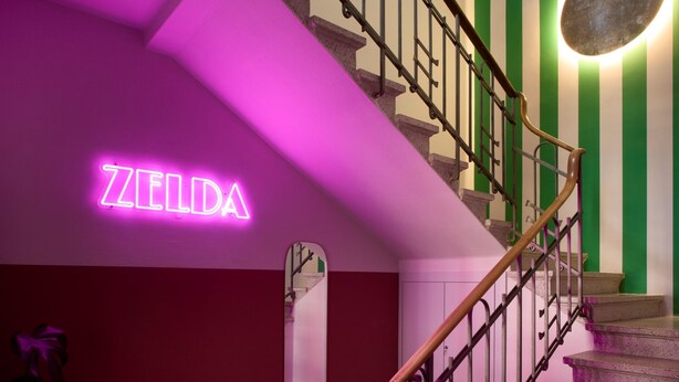 Un escalier orné d’un panneau néon sur lequel on peut lire « ZELDA » et d’un miroir accroché au mur.