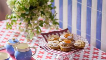 A table with a red and white checkered tablecloth, a glass serving tray with pastries, and blue cups and saucers.