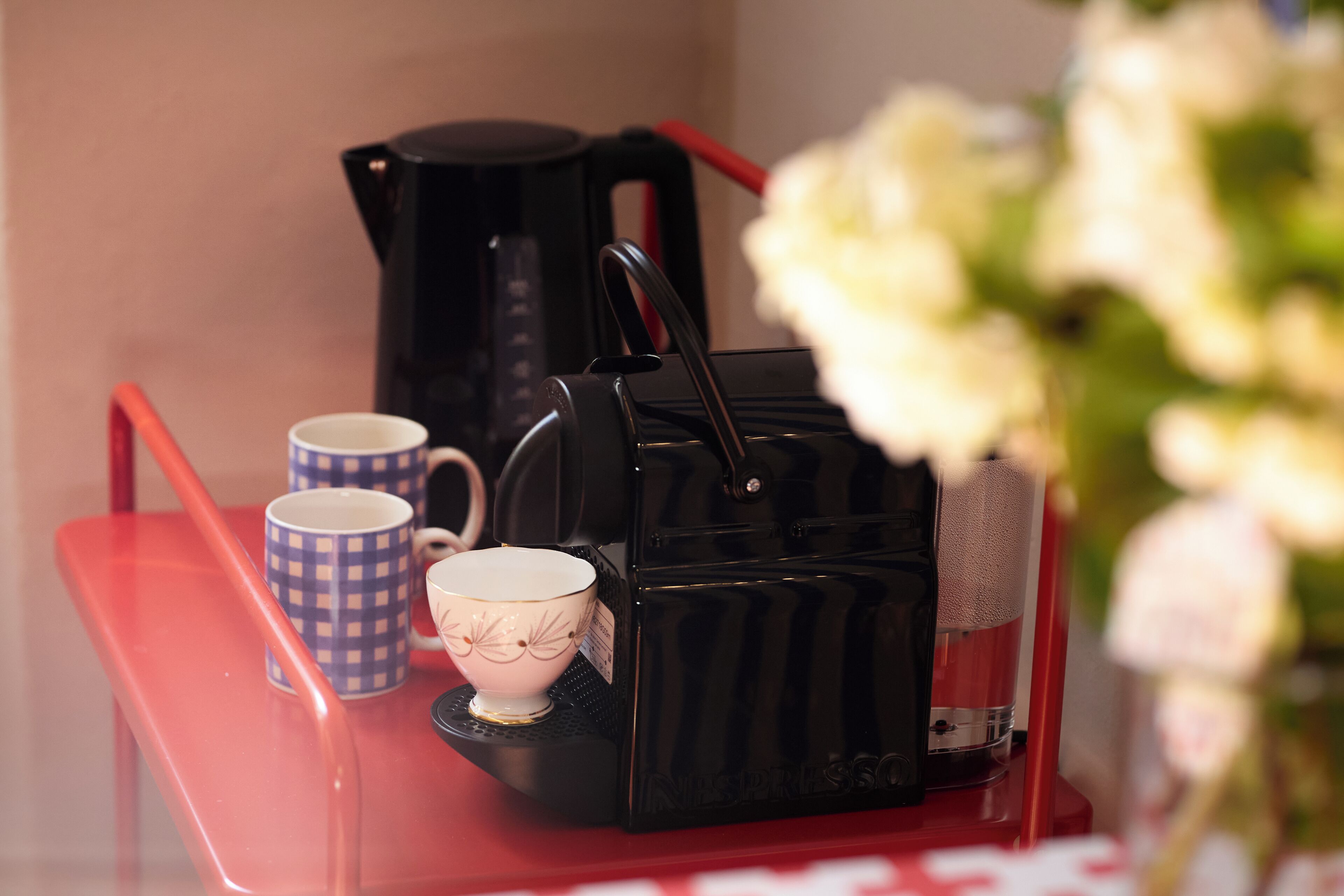 A coffee maker on a red tray with two cups, one with a checkered pattern and another plain.
