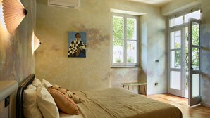 Une chambre à coucher avec un lit, des oreillers, un tableau, un appareil de climatisation et une fenêtre donnant sur un paysage verdoyant.