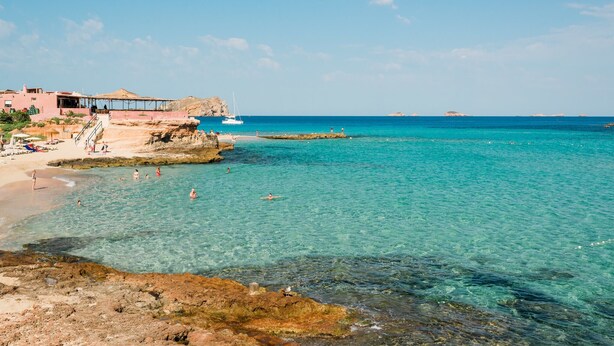 Un hotel frente al mar con playa, aguas turquesas cristalinas y terreno rocoso.
