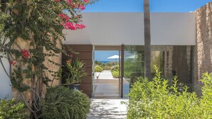 Un edificio moderno con entrada de vidrio, un camino hacia un patio y vista al océano.