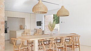 Una cocina moderna con armarios blancos, una mesa de comedor de madera y lámparas colgantes de mimbre.
