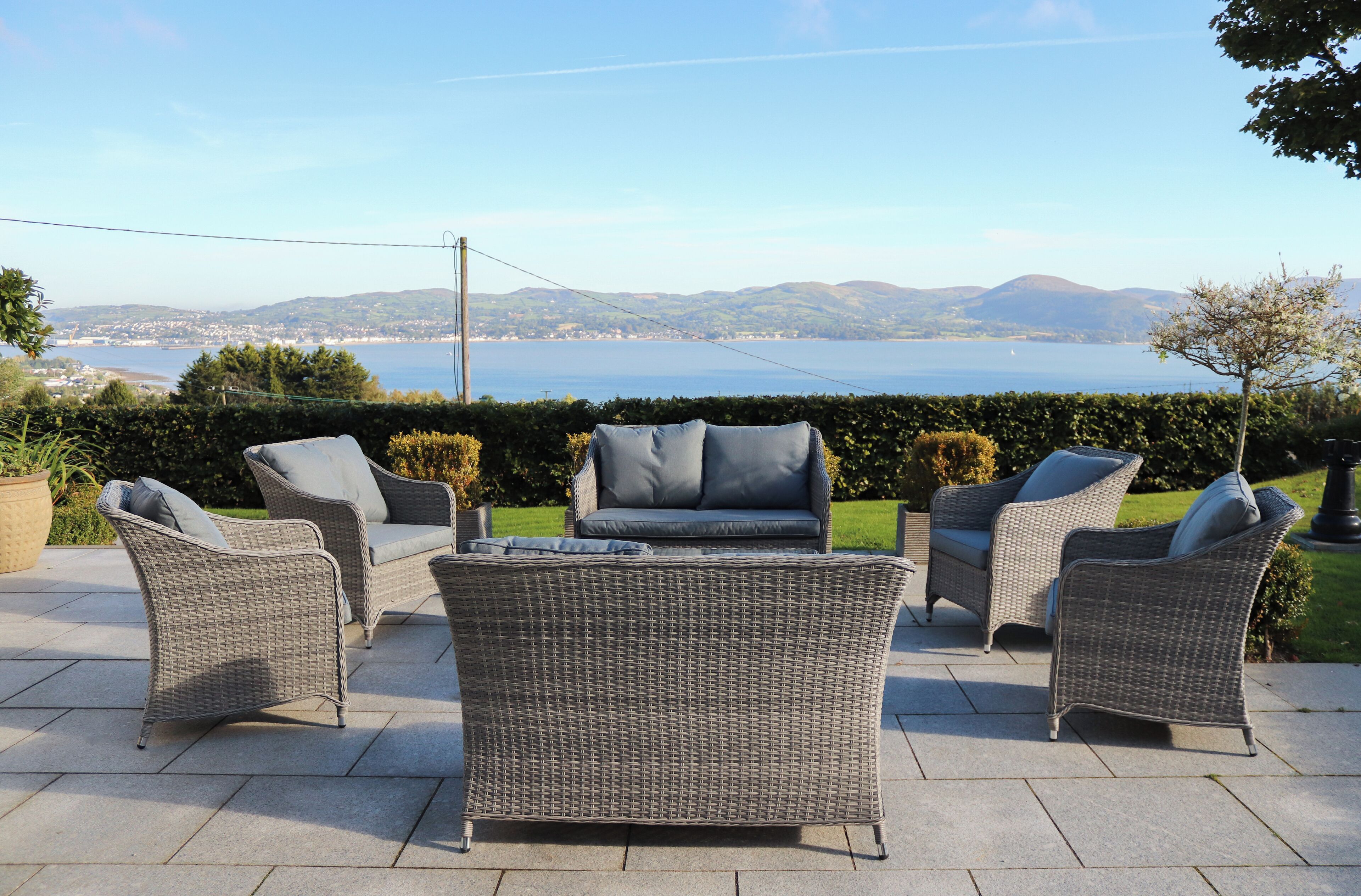 Outdoor wicker furniture with cushions, arranged on a patio with a scenic view of a lake and distant hills.