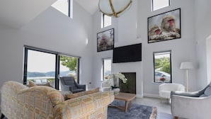 Un salon moderne avec un canapé, des fauteuils, une cheminée et de grandes fenêtres donnant sur un paysage.