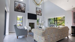Un salon spacieux avec un canapé à motifs, un fauteuil gris et un téléviseur à écran plat fixé au mur.