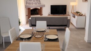 A modern living room with a stone fireplace, a flat-screen TV, and a dining area with white chairs and a wooden table. - Coquet 3 Pièces vue mer (Cagnes-sur-Mer)