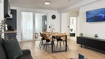 A modern living space with a dining area, a sofa, a TV, and a kitchen area.