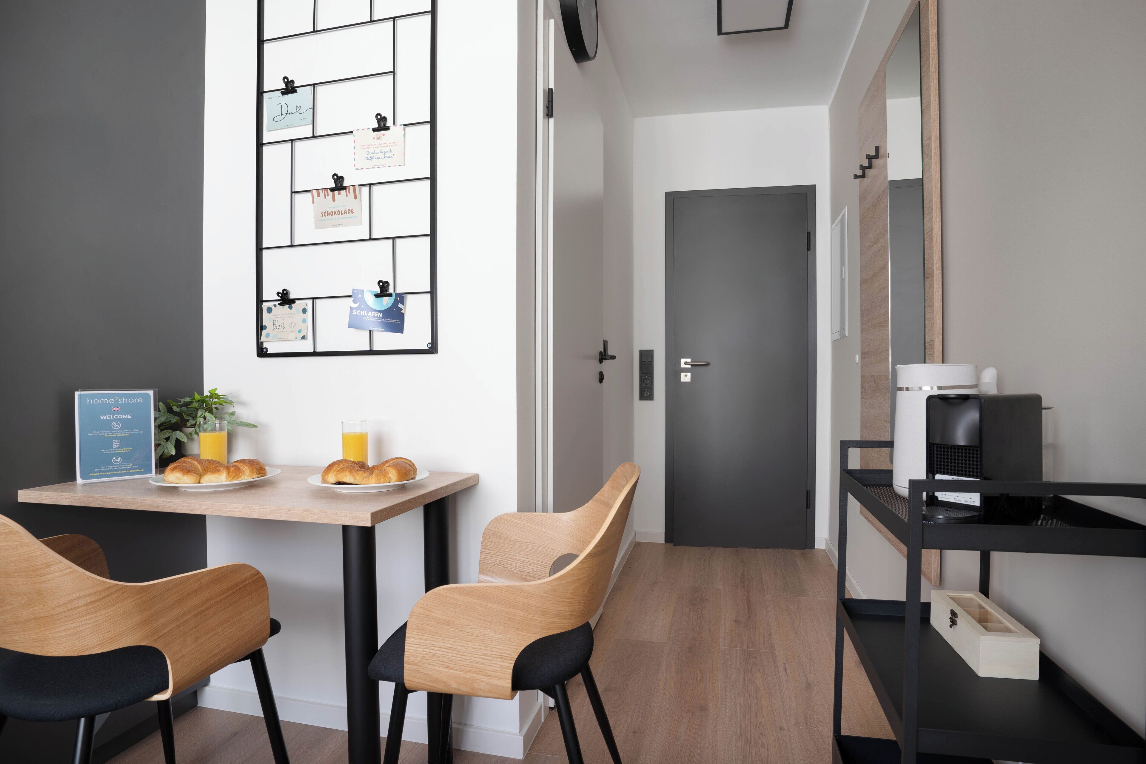 Una cucina moderna con un tavolo in legno, due sedie, una macchina da caffè e una bacheca a parete.