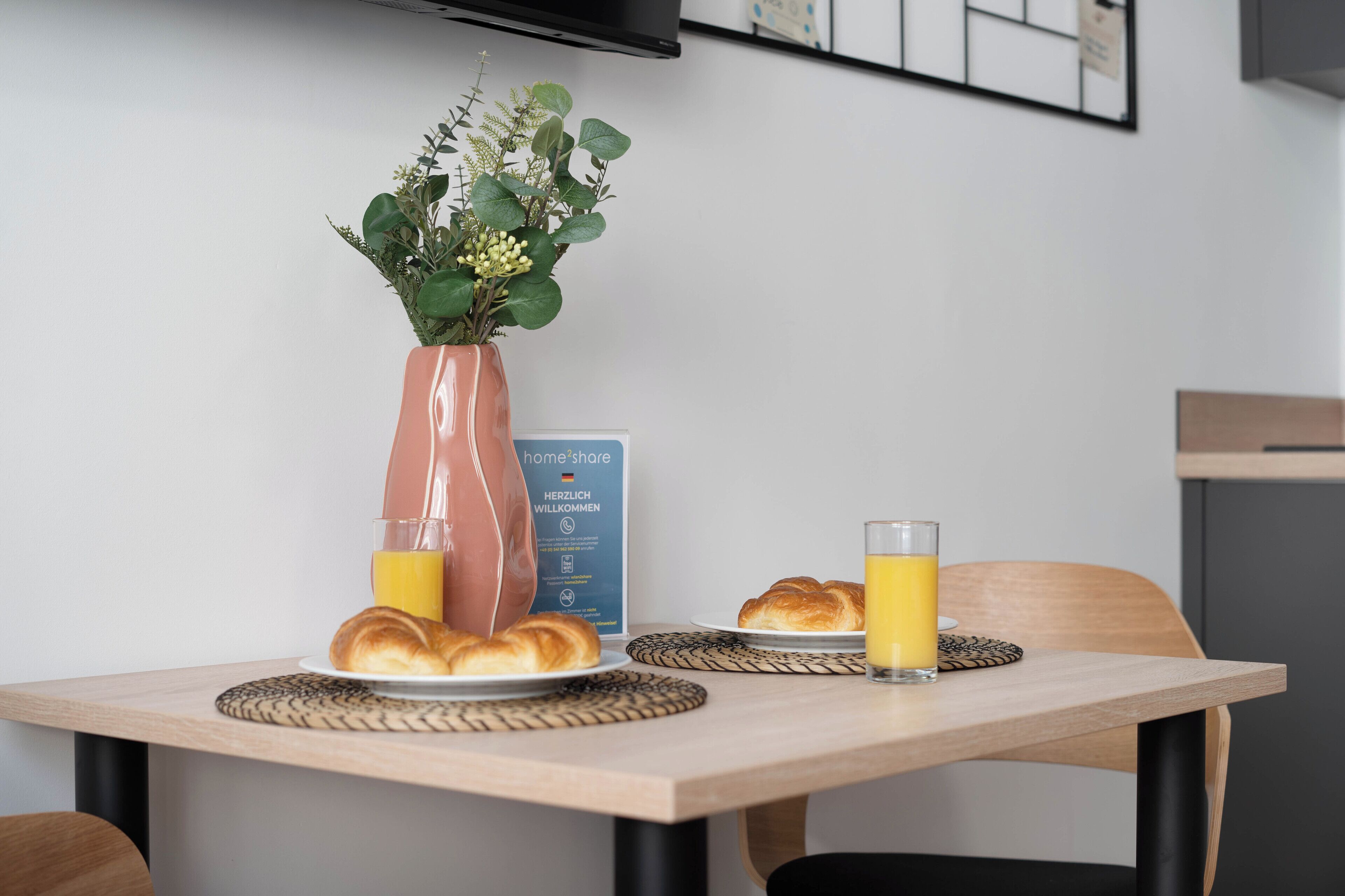 Een ontbijttafel met croissants, een vaas met groen en een glas sinaasappelsap.
