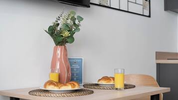 Een ontbijttafel met croissants, een vaas met groen en een glas sinaasappelsap.