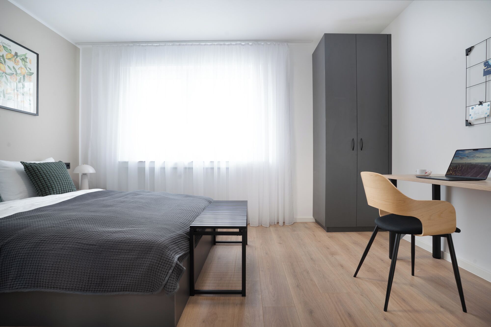 Una camera da letto moderna con un letto, una scrivania con un portatile, una sedia e un armadio.