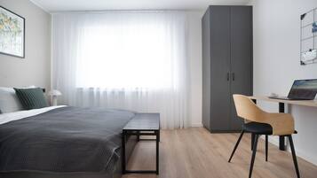 Una camera da letto moderna con un letto, una scrivania con un portatile, una sedia e un armadio.