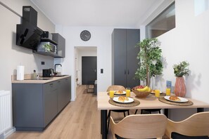 A modern kitchen with grey cabinets, a built-in stove, and a dining area with a wooden table set for breakfast. - Central Bonn Apartments I home2share (Bonn)