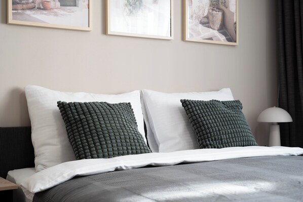 A neatly made bed with white and green pillows, a grey blanket, and a lamp on a bedside table. - Central Bonn Apartments I home2share (Bonn)