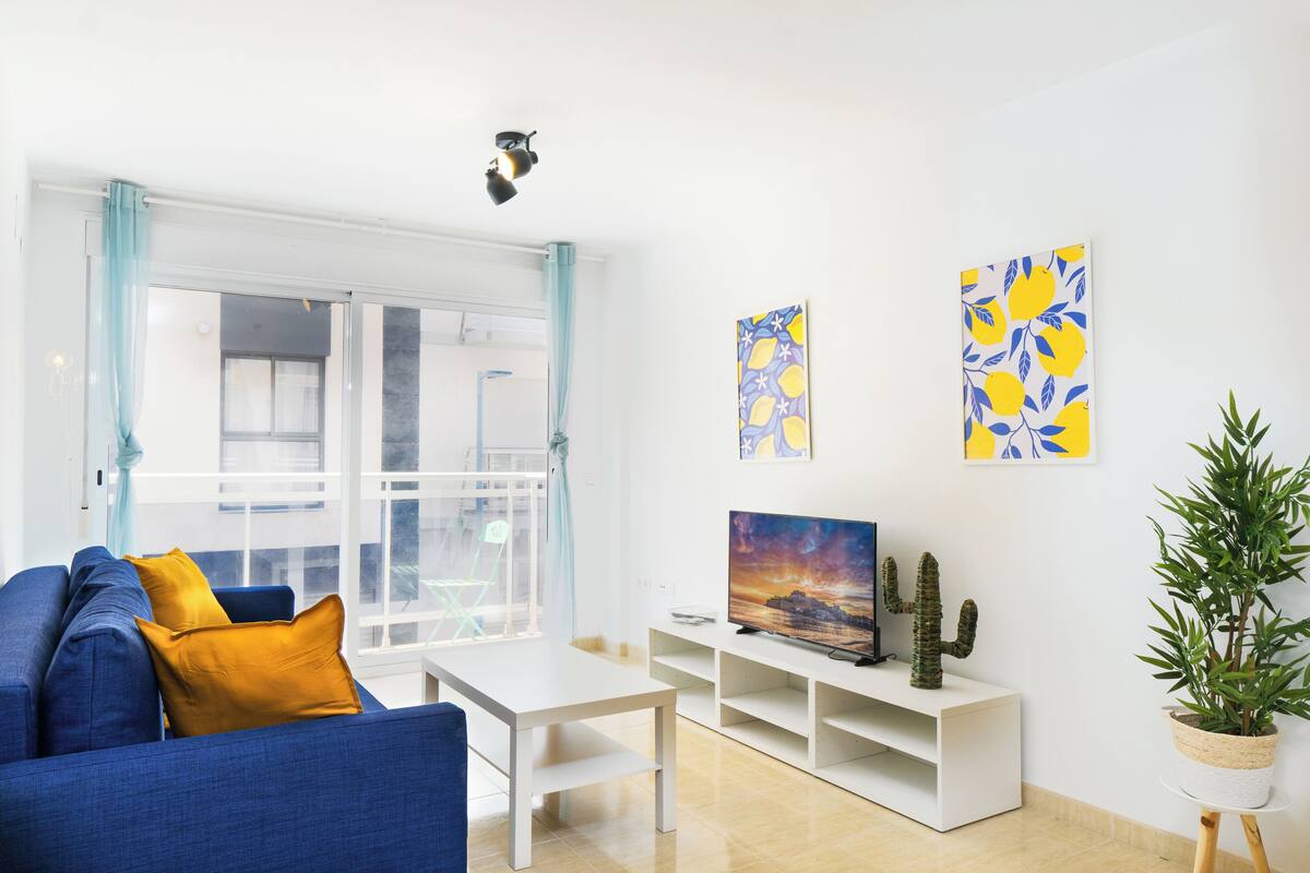 A modern living room with a blue sofa, white coffee table, and artwork on the walls.